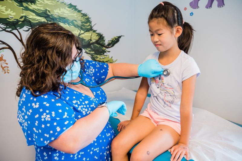 a medical provider listening to the heart of a young girl with a stethoscope